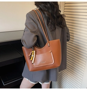Dettaglio della borsa tote marrone caramello con texture a grana e ciondolo di perline