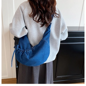 Detailansicht einer dunkelblauen Denim-Halbmondtasche mit Falten-Design getragen am Modell