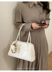 Detail of cream shoulder bag with plush ball charm and minimalist retro design