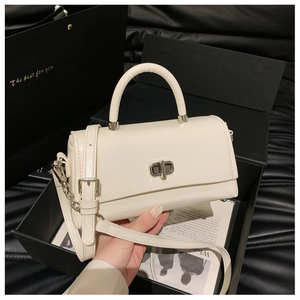 Detail of a creamy white handbag featuring a silver twist lock and elegant gift packaging