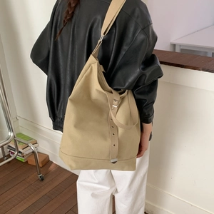 Détail du sac cabas en toile kaki avec œillets métalliques porté par un mannequin