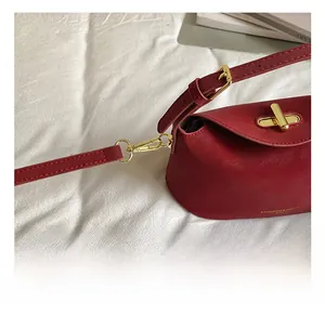 Detail of red leather pillow bag with gold metal hooks and buckle on white fabric