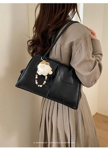 Minimalist black leather underarm bag with plush ball charm shown in a model lifestyle shot