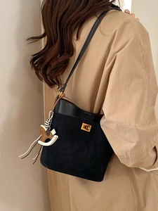 Minimalist black bucket bag with gold clasp and rocking horse charm on a beige coat model