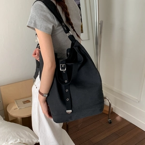 Détail du sac à bandoulière en toile noire montrant la sangle et les œillets en métal