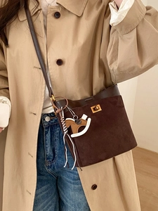 Brown suede bucket bag with gold lock and horse charm worn with a stylish trench coat