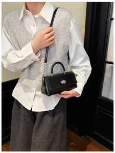 Close-up of black glossy handbag with silver turn-lock and leather chain strap