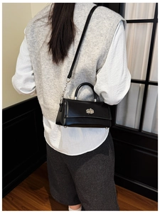 Model wearing a black leather crossbody bag with silver chain and metal clasp