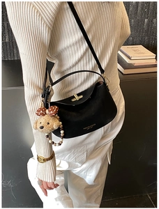 Detail of black matte leather pillow bag with gold clasp and plush bear charm