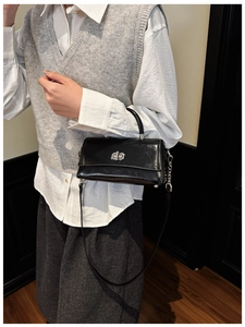 Detailed view of black patent leather crossbody bag with silver twist lock and slim strap