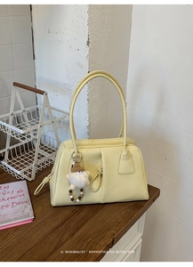 Detail view of light yellow faux leather shoulder bag with a white plush doll pendant