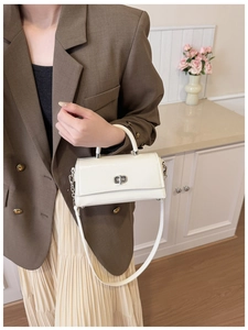 Close-up of elegant white crossbody bag with silver twist lock on a model in home setting
