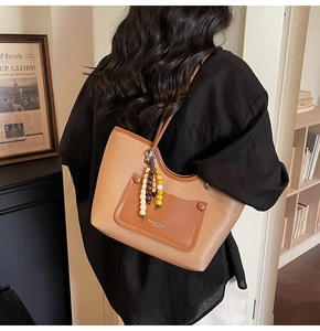 Dettaglio borsa tote in pelle marrone con tasca a contrasto e ciondolo di perline decorativo