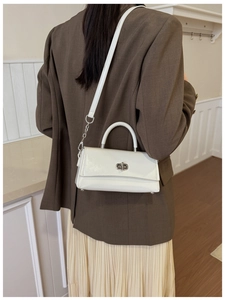 Close-up of white minimalist shoulder bag with silver clasp and metallic chain strap detail