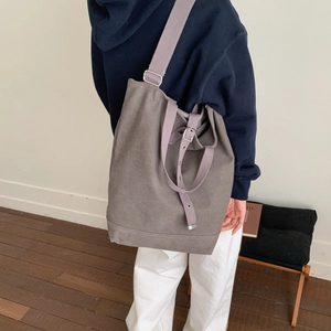 Gros plan sur un sac seau en toile grise avec une bandoulière large violette réglable