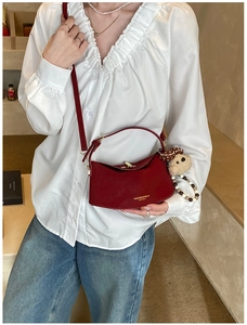 Close-up of a burgundy leather handbag with gold twist lock and a cute bear charm