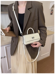 White minimalist crossbody bag with silver twist lock shown on model with brown blazer