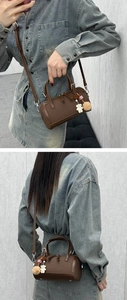 Detail view of brown pebbled leather Boston bag with cute bear and pompom bag charm
