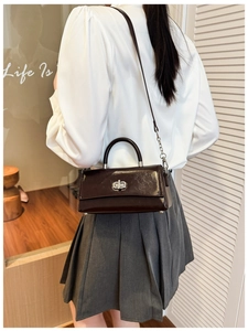 Detail of dark brown patent leather handbag with silver metal buckle and chain strap