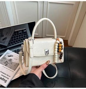 Detail of cream crossbody bag with silver twist lock and decorative wooden bead charm
