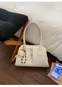 Detail of a creamy white leather tote bag with a cute charm on a dark wood floor