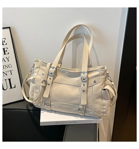 Detail view of cream leather tote bag featuring silver buckles and side zipper pocket