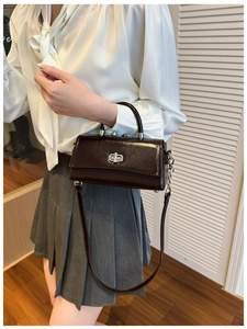 Detail view of a chocolate brown glossy leather handbag with silver twist lock and strap