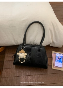 Detail of black leather underarm bag with a cute wood bead and plush charm accessory