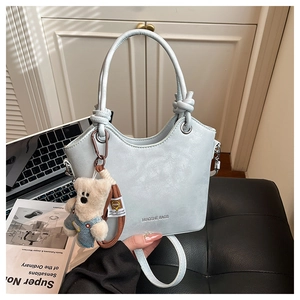 Close-up of light blue bucket bag featuring a plush bear charm and knotted handle details