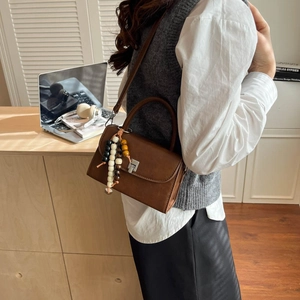 Detailed view of a brown vintage leather bag with silver buckle and ethnic bead charm