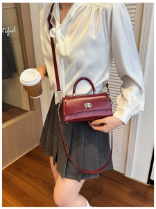Detail of burgundy glossy leather handbag with silver lock and adjustable shoulder strap