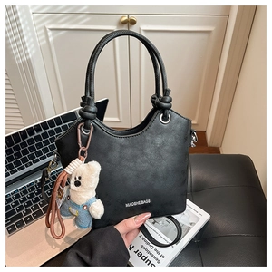 Detail of black leather bucket bag with decorative knot handles and cute bear charm