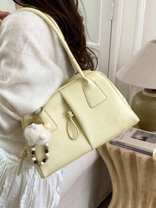 Minimalist cream shoulder bag with knot detail and plush pendant in casual home setting