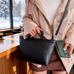 Detail of black matte leather tote bag with handle and strap in a cozy cafe setting