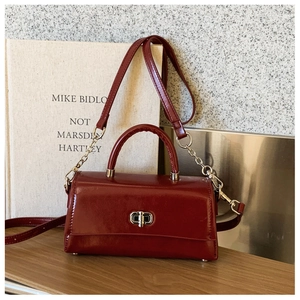Macro view of burgundy glossy leather handbag with silver twist lock on wood table