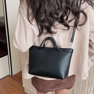 Detail of black faux leather tote bag with dual handles and adjustable strap on a model