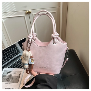 Pink lychee leather bucket bag with cute bear charm on a desk with a laptop