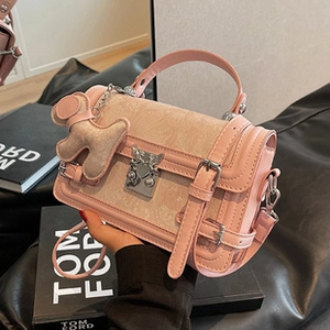 Detail of pink leather tote bag with floral embossing, metal buckle, and doll charm