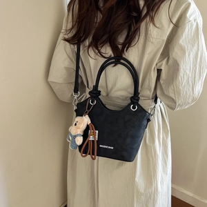 Minimalist black leather bucket bag with cute bear charm worn with a beige trench coat