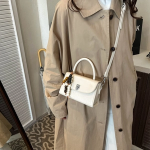 Detailed view of cream crossbody bag with wooden beads and elegant metal swivel lock