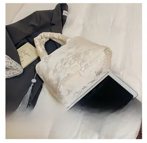 Détail de la broderie florale sur un sac en satin avec pompon gris et ornement de jade