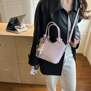 Detail of pink bucket bag with knot handle and plush bear charm on a wooden desk