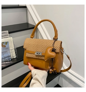 Close-up of brown leather handbag featuring herringbone weave and heart charm