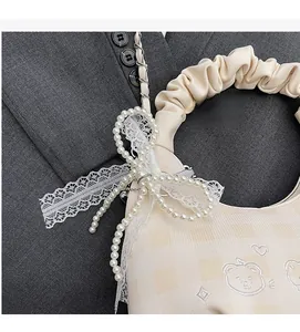 Detail of cream pleated handle bag featuring pearl bow and delicate bear embroidery