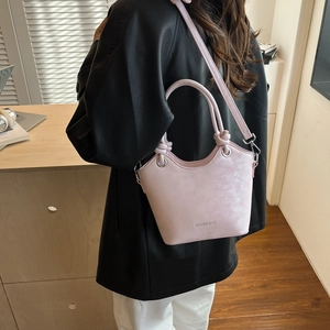 Model wearing a light pink bucket bag with knot handle and silver hardware