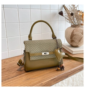 Detail of olive green handbag with herringbone fabric, silver clasp and heart tassel charm