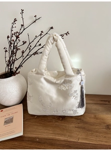 Détail de broderie florale élégante sur sac en soie beige avec pompon gris de luxe