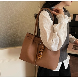 Detail of caramel brown tote bag with leather texture and wooden bead pendant accessory