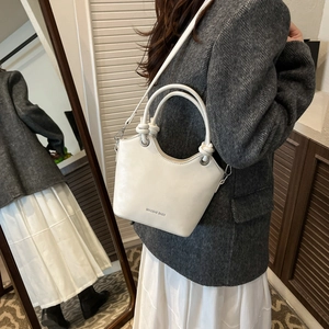 Detail of white bucket bag with wavy rim, held by model in a grey suit and white dress