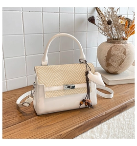 Close-up of woven flap and silver metal twist lock on a beige crossbody square bag